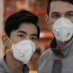 Two workers wearing NIOSH-certified respirator masks in an industrial warehouse