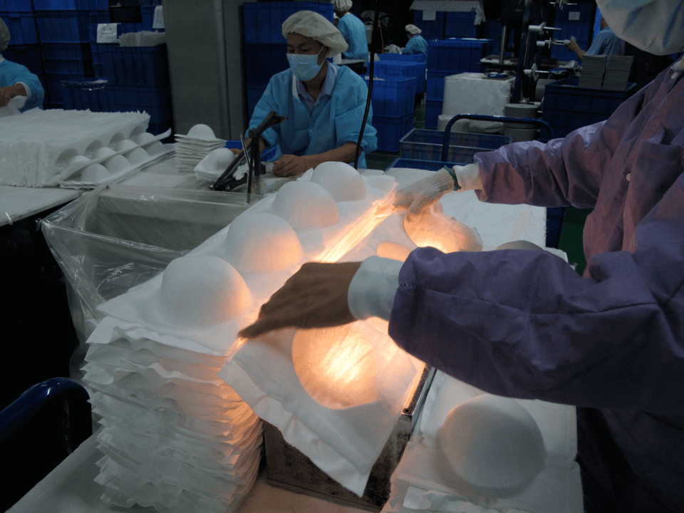 Factory worker performing light-assisted quality control inspection on Makrite N95 cone respirator masks